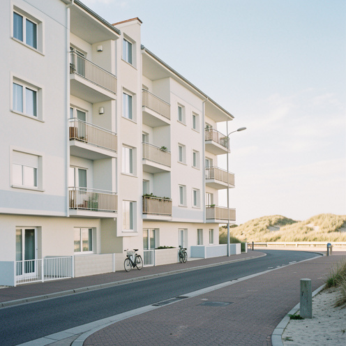 Immeuble d appartements lumineux près de la promenade maritime de Cayeux-sur-Mer, avec des façades claires, des balcons et les dunes en arrière-plan.